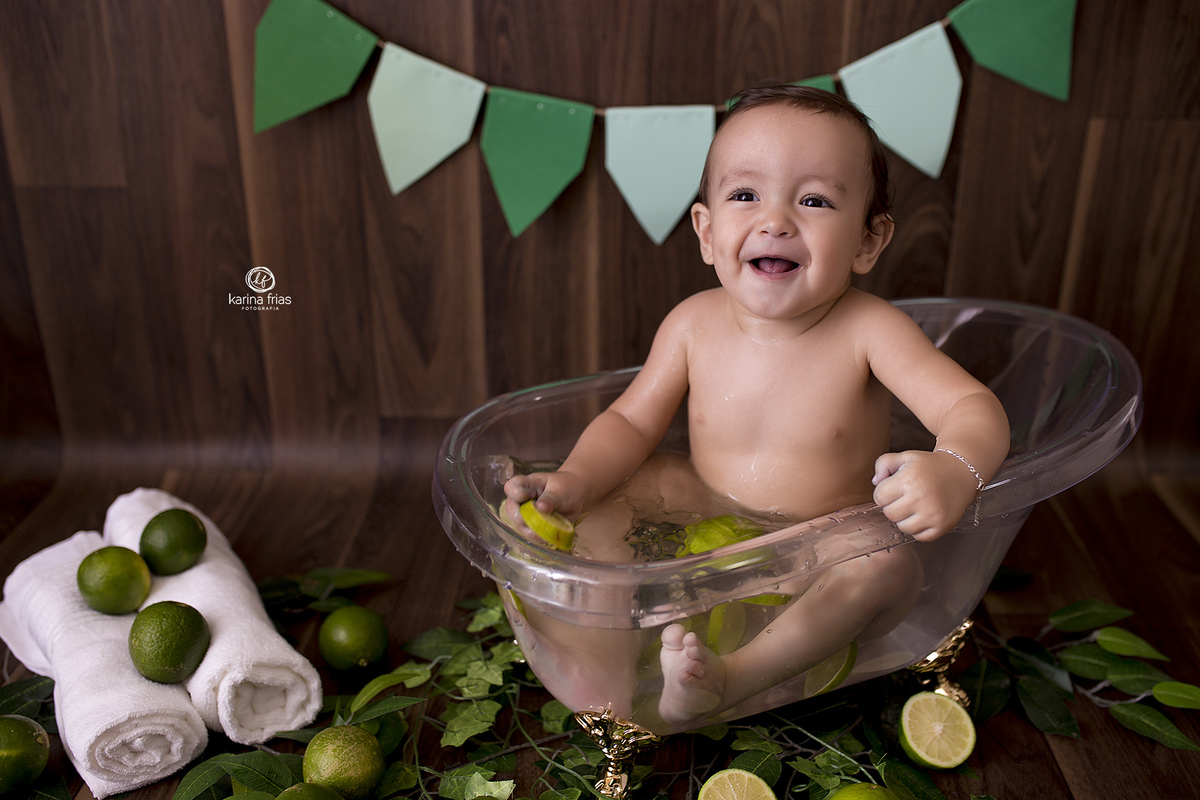o menino sorri dentro da banheira para as fotos de um aninho