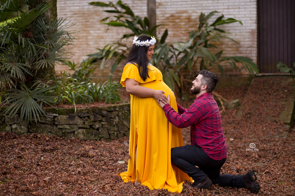 o pai se ajoelha para a gestante na sessão de fotos