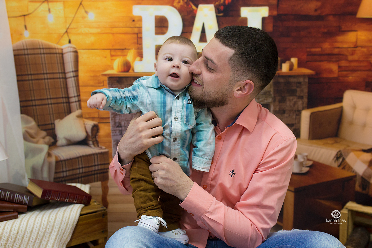 o pai beija a criança que olha para  fotografa de bebes de caxias do sul, karina frias