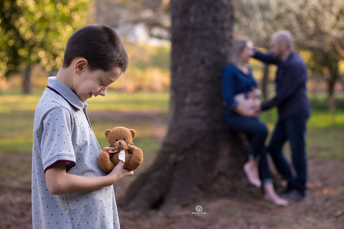 os pais ficam desfocados enquanto o irmao olha para o ursinho do bebe