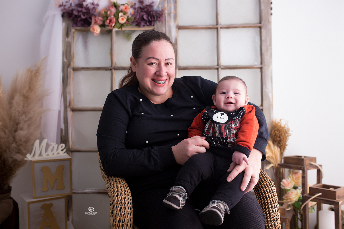 o menino sorri no colo da mae na sessão de fotos