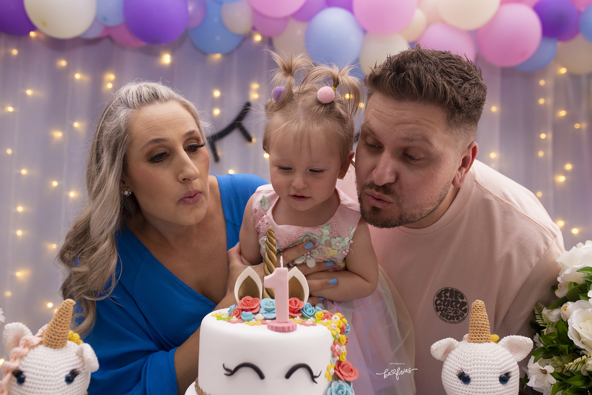 os pais assopram a velinha na festa de aniversario da filha