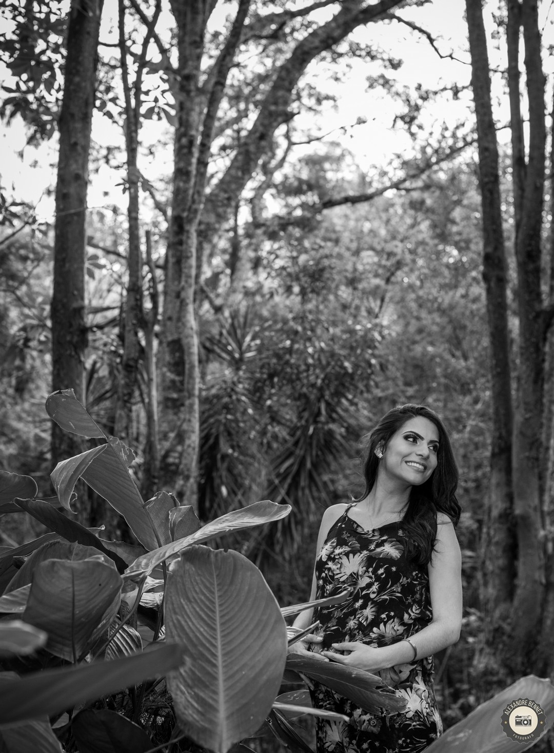 Belo registro em preto e branco da gestante com as mãos sobre a barriga e com um grande sorriso no rosto 