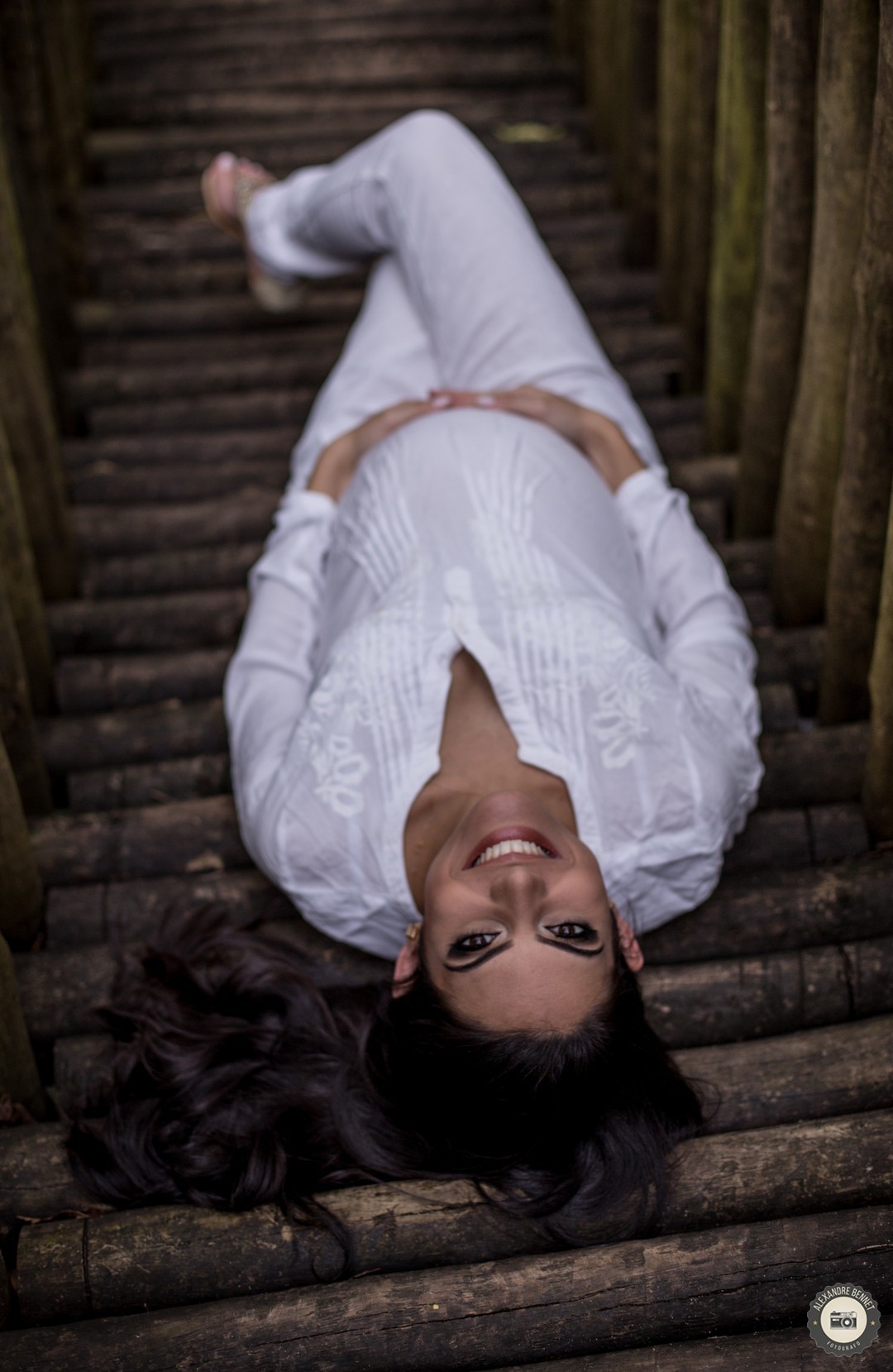 Deitada em uma ponte de madeira a gestante olha para o fotógrafo e da um belo sorriso uma foto perfeita de um ensaio de gestante 