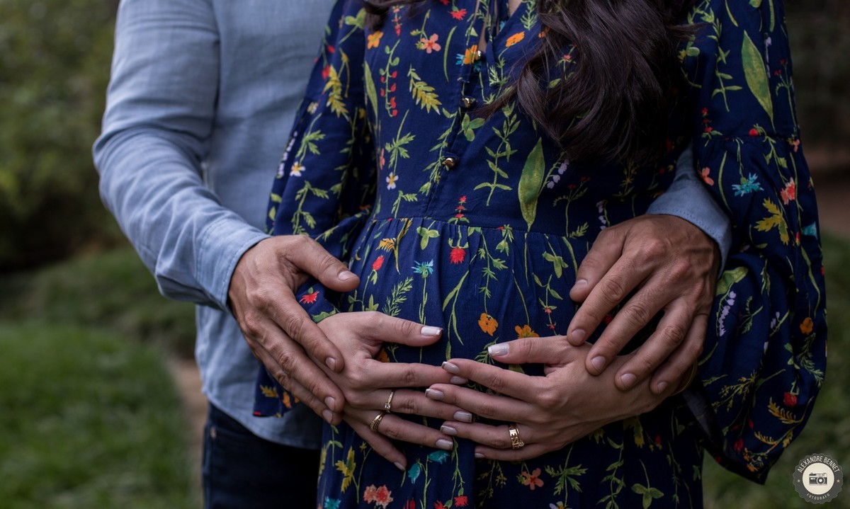Belo detalhe da barriga da gestante envolvida por suas mãos e pelas mãos de seu marido