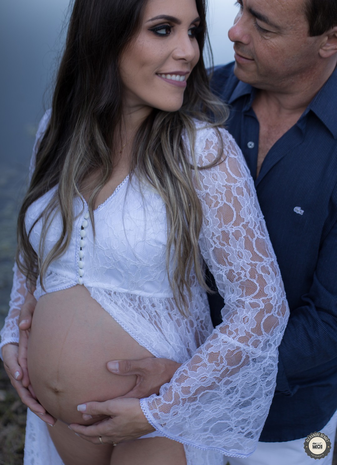 Pai abraça gestante por trás e coloca as mãos sobre sua barriga 