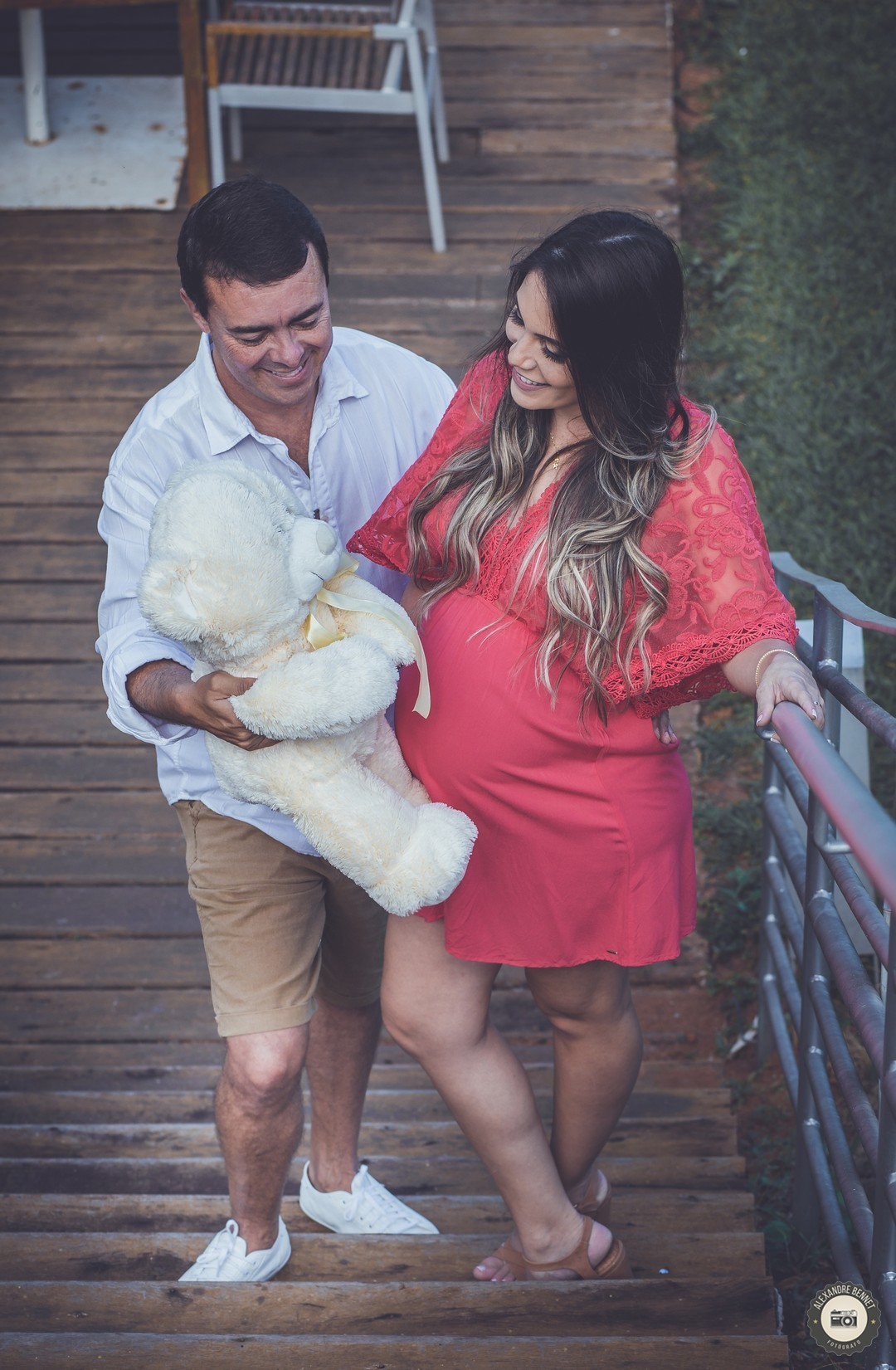 Segurando o ursinho do bebê o casal se olha e abre um belo sorriso 