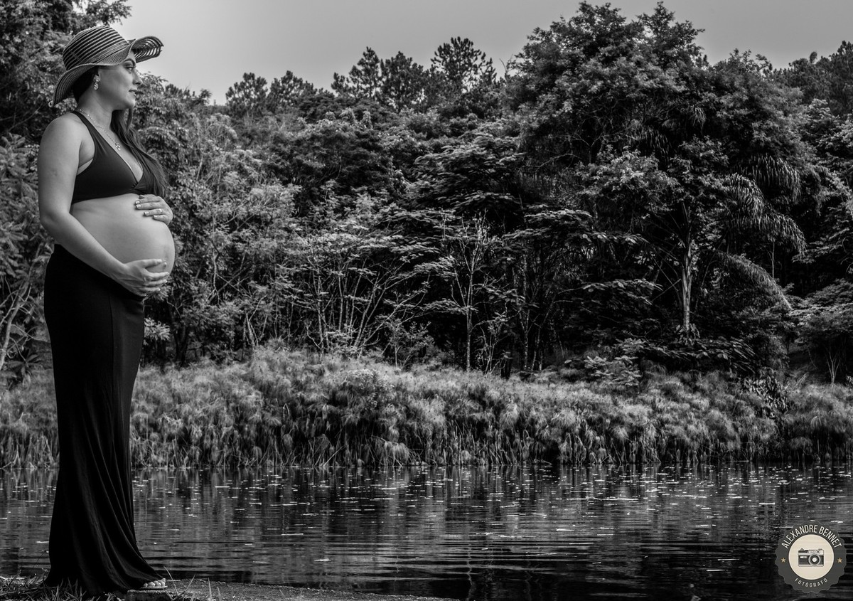 Gestante olha para o horizonte na beira de uma lagoa em uma bela foto preta e branca