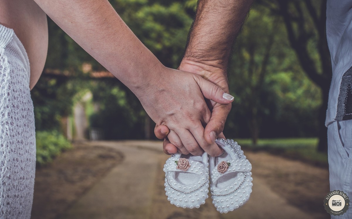 Detalhe das mãos do casal segurando os sapatinhos do bebê 