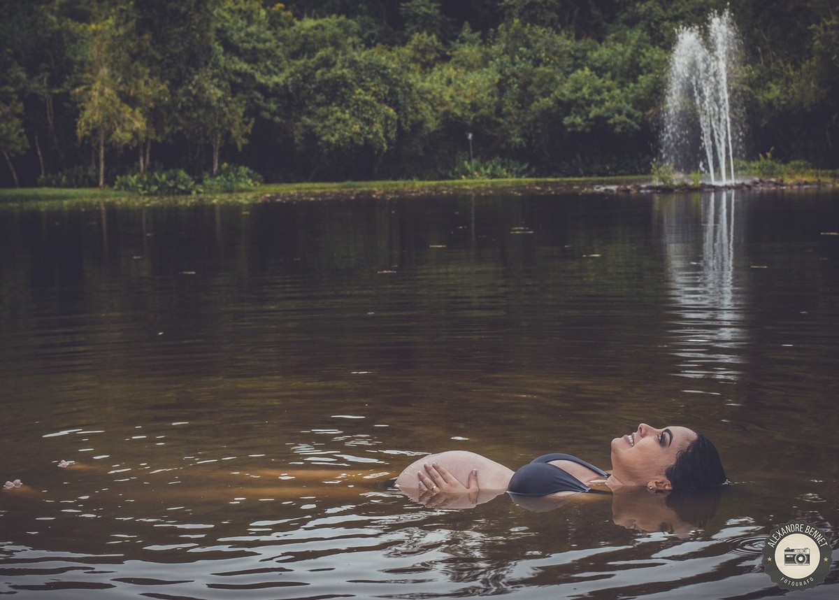Grávida dentro da água deita e olha pra cima imaginando seu bebê