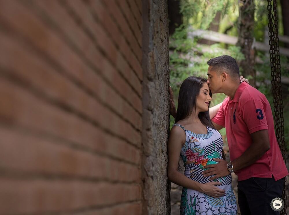 Com as mãos na barriga da gestante o pai chega e lhe da um beijo na testa 
