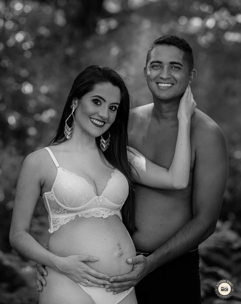 Pai abraça a gestante por trás com as mãos em sua barriga e os dois dão um belo sorriso