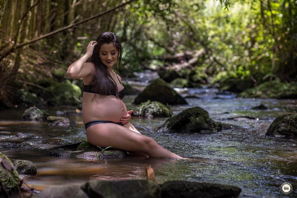 Grávida sentada na pedra de uma cachoeira pensando em seu bebê 
