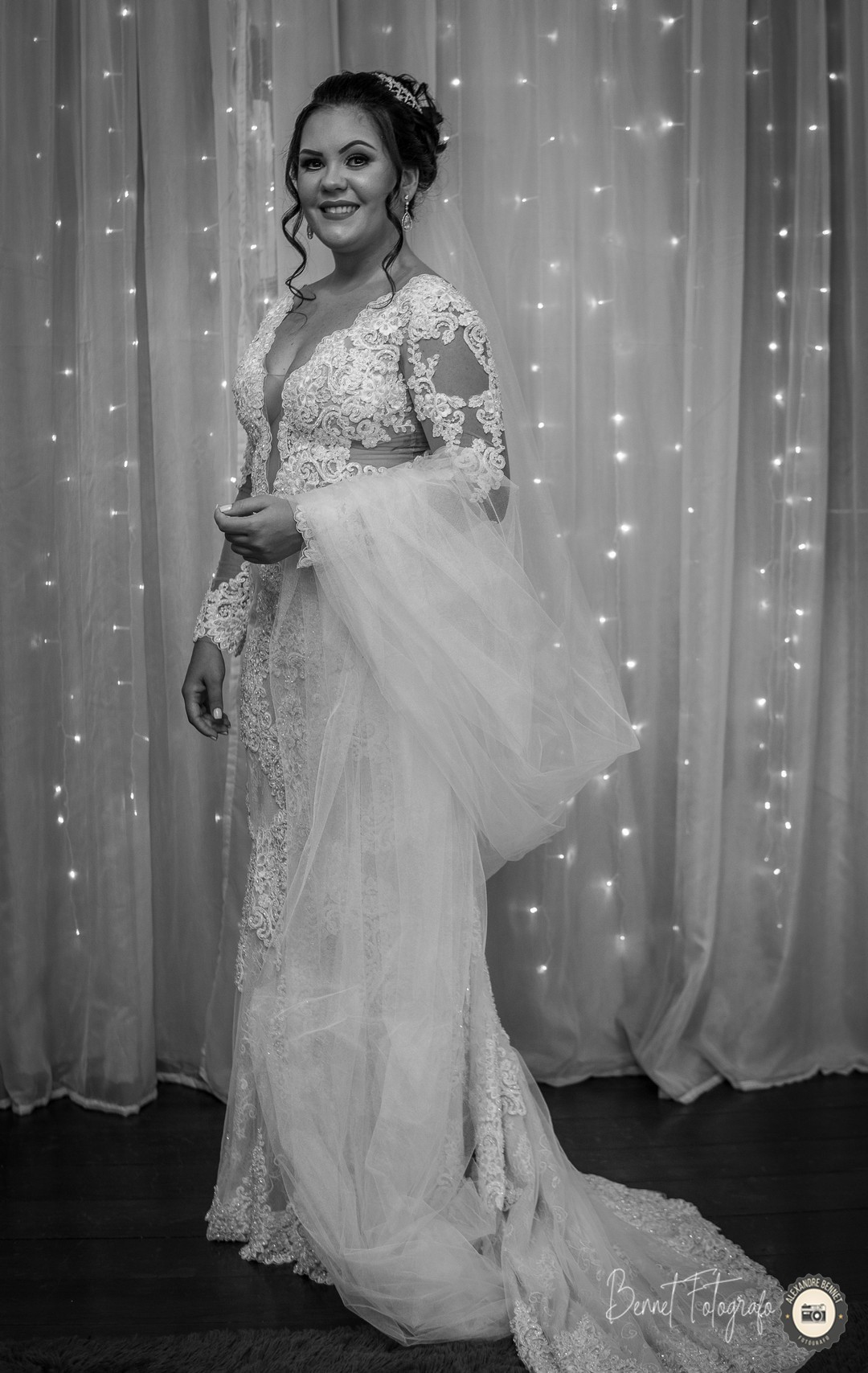 Com um grande sorriso noiva posa para foto com seu belo vestido e o grande véu no braço