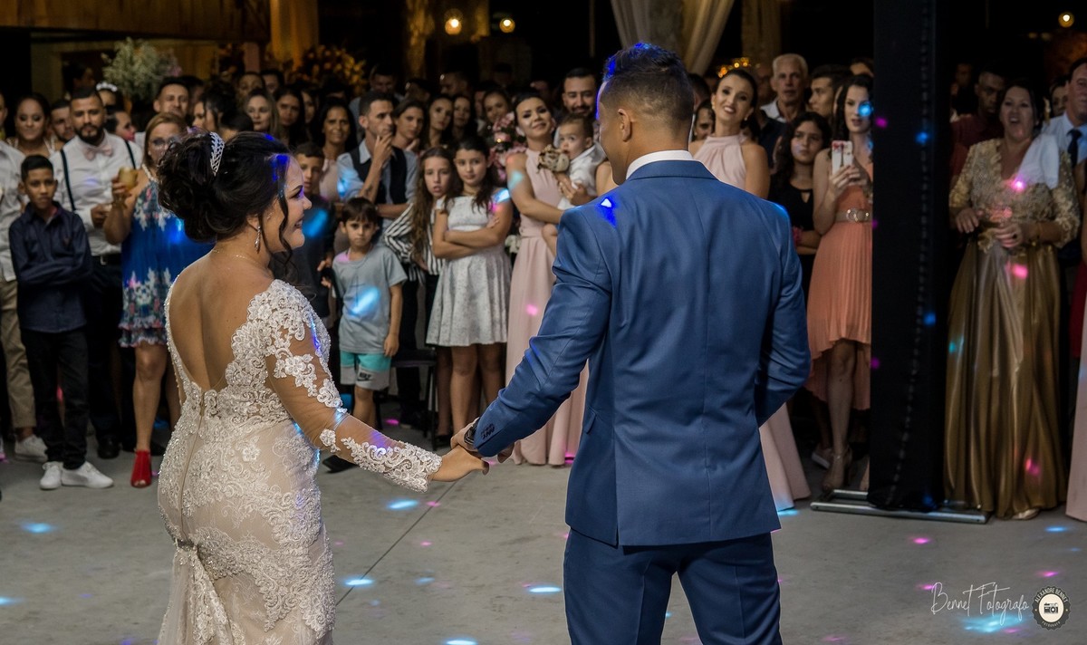 Casal de mãos dadas na hora da valsa com o público muito emocionado ao fundo 