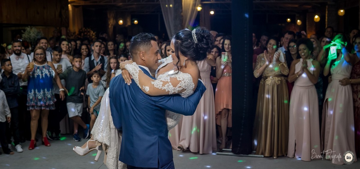 Noivo com a noiva nos braços durante a valsa num ato de cavalheirismo e o público aplaude ao fundo 