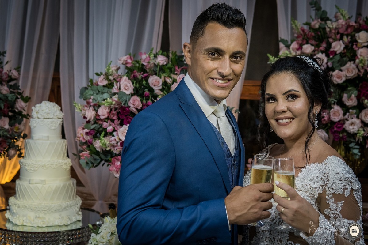 Casal em frente a mesa do bolo brindando toda a felicidade do momento 