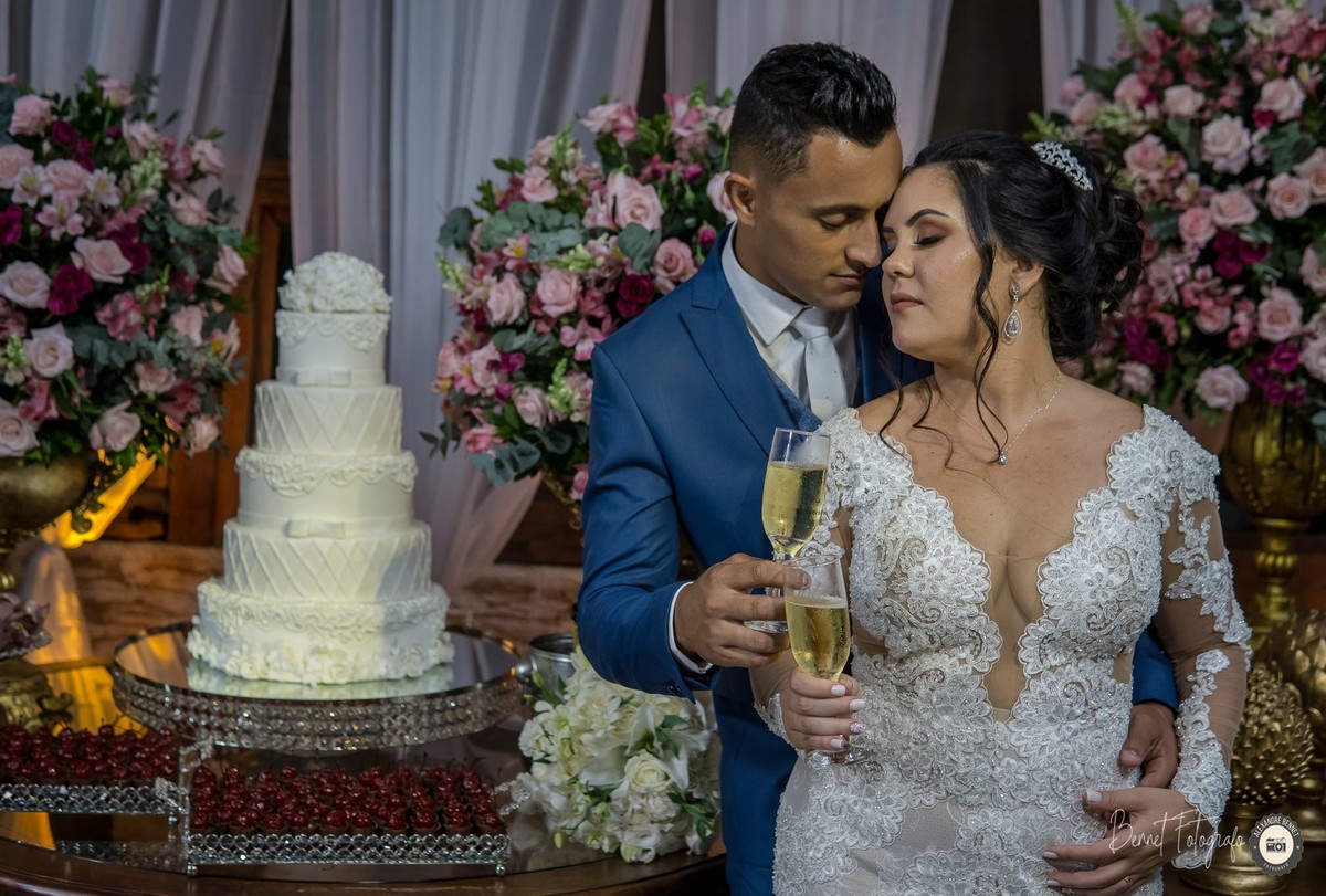 Noivo e Noiva de olhos fechados na frende da belíssima mesa do bolo fazendo o brinde 