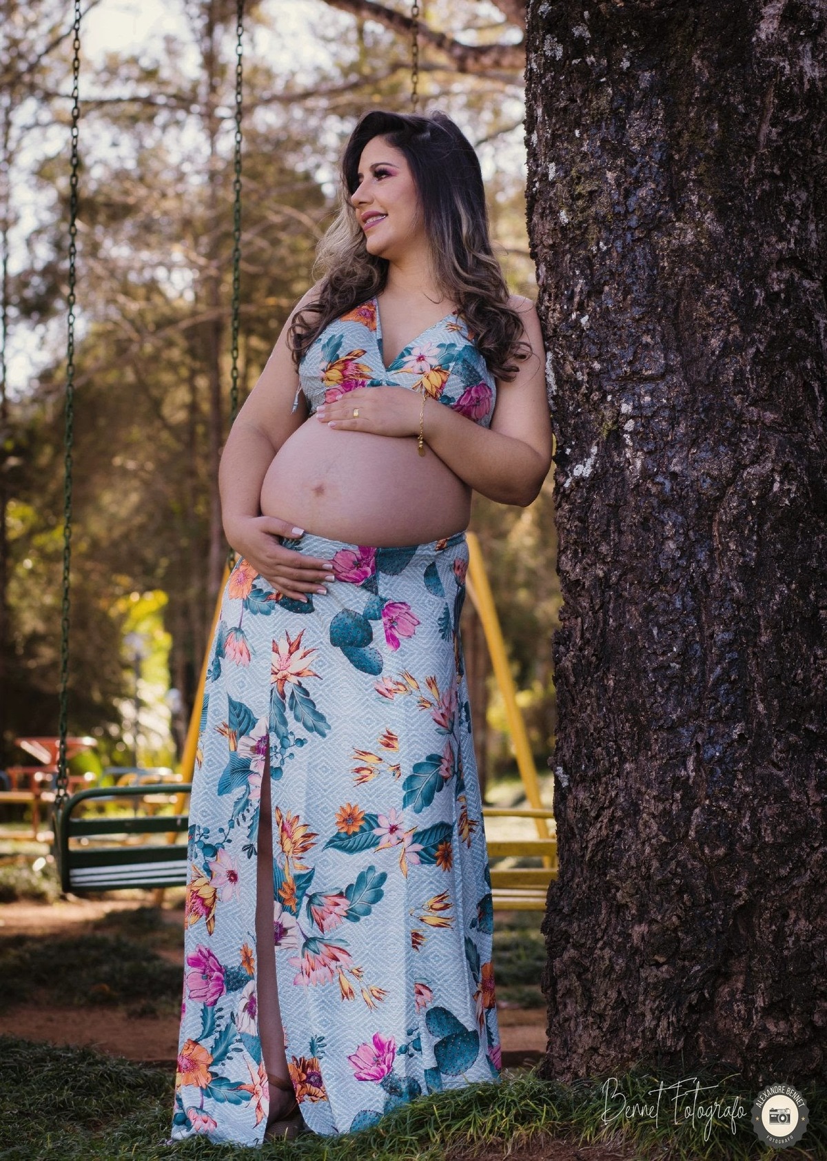 Gestante se encosta na árvore com as mãos na barriga 