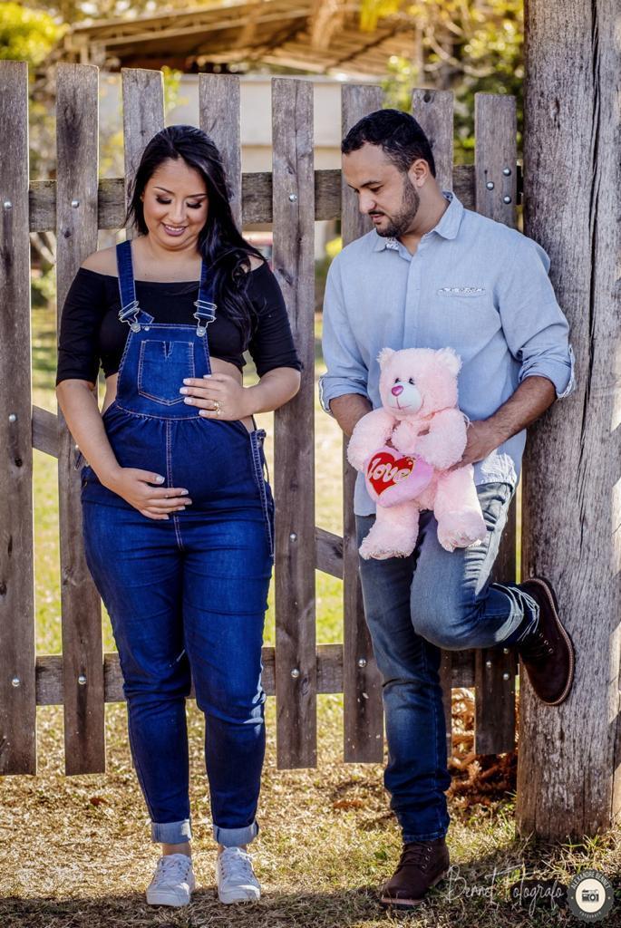 casal se encosta na cerca enquanto pai segura um ursinho 