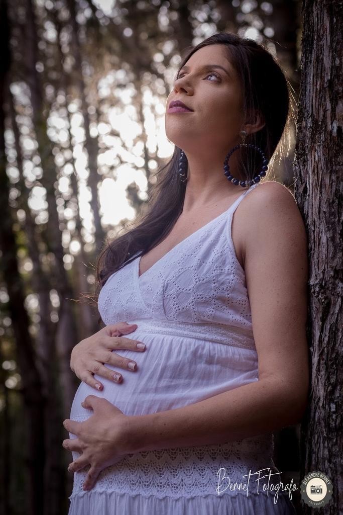Mãe se encosta na árvore com as mãos na barriga e olha para cima