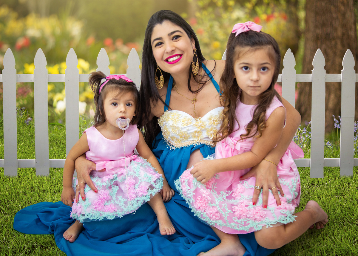 book de gestante registrado pelo fotografo marcos toledo, foto que mostra as maninhas com vestidos cor de rosa sentadas no colinho da mamae que espera a chegada do maninho