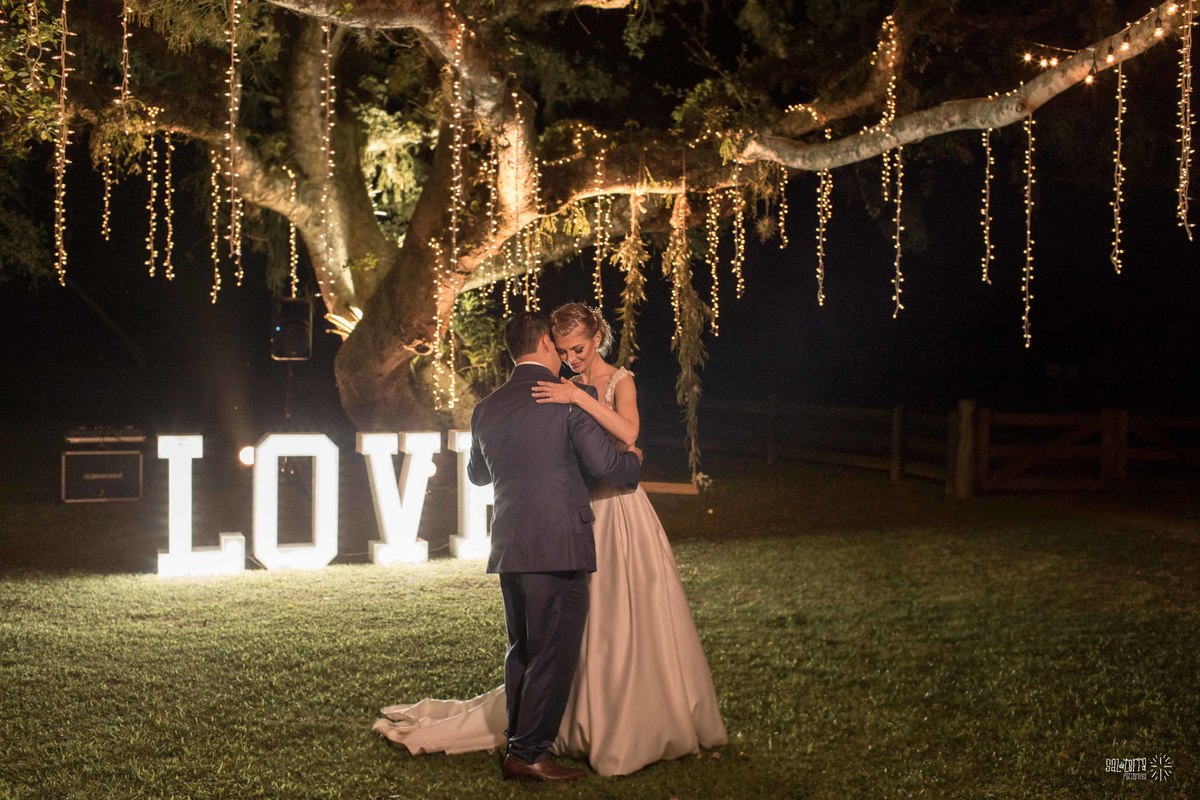 casamento ao ar livre em baixo da figueira alto da capela porto alegre entrada da noiva vestido marco tarrago traje franzn alfaiataria decoracao cor de perola varau de luzinhas em baixo da figueira love luminoso fotografo de casamento no brasil