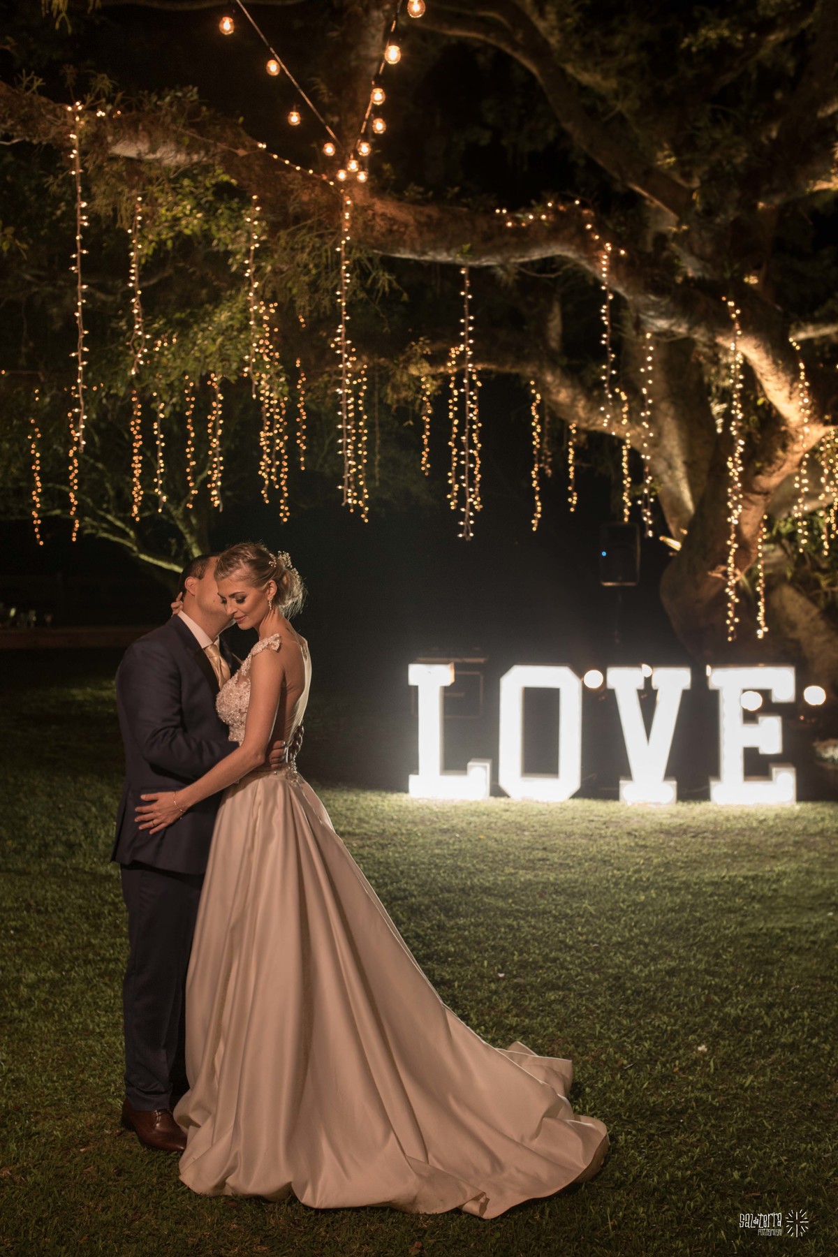 casamento ao ar livre em baixo da figueira alto da capela porto alegre entrada da noiva vestido marco tarrago traje franzn alfaiataria decoracao cor de perola varau de luzinhas em baixo da figueira love luminoso fotografo de casamento no brasil