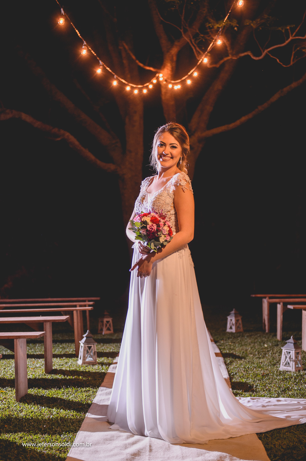 Noiva posando com seu bouquet sob as luzes da figueira.