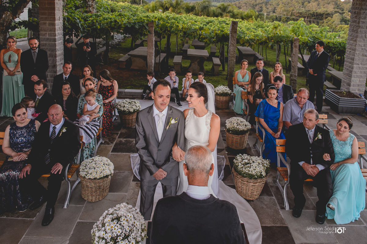 Vista frontal dos noivos diante do juíz de paz e seus convidados ao fundo. 