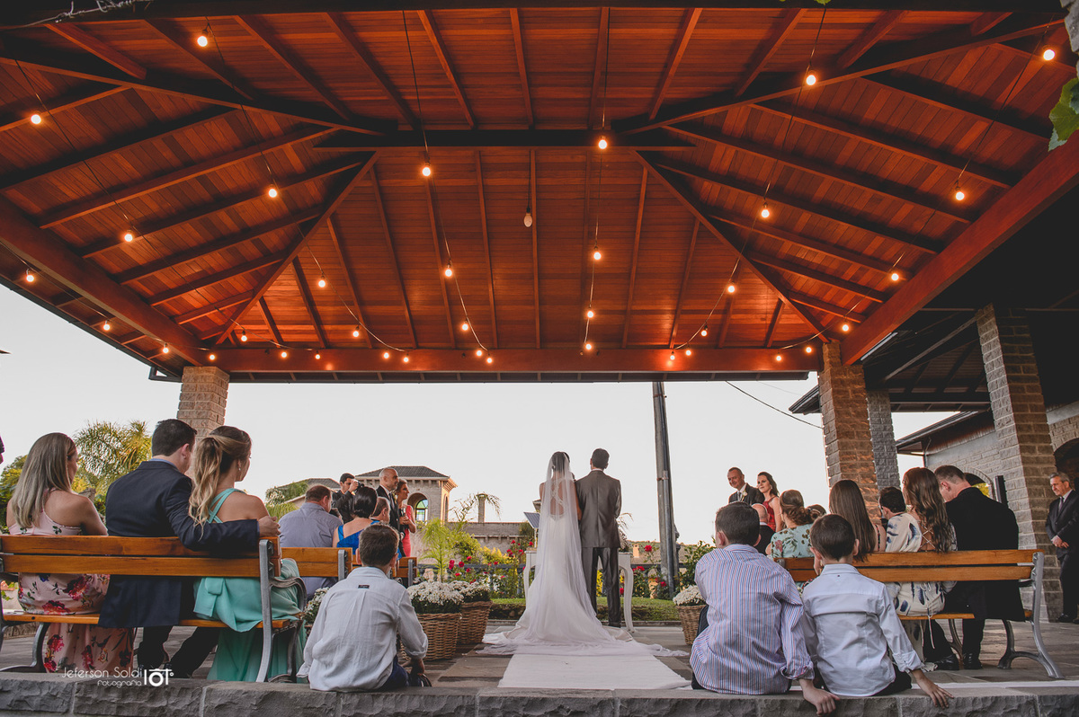 Vista dos noivos no altar sendo observados por seus convidados.