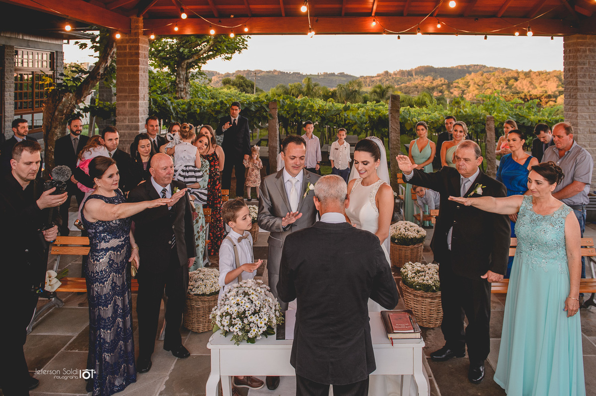 Convidados estendem o braço direito para a benção das alianças.