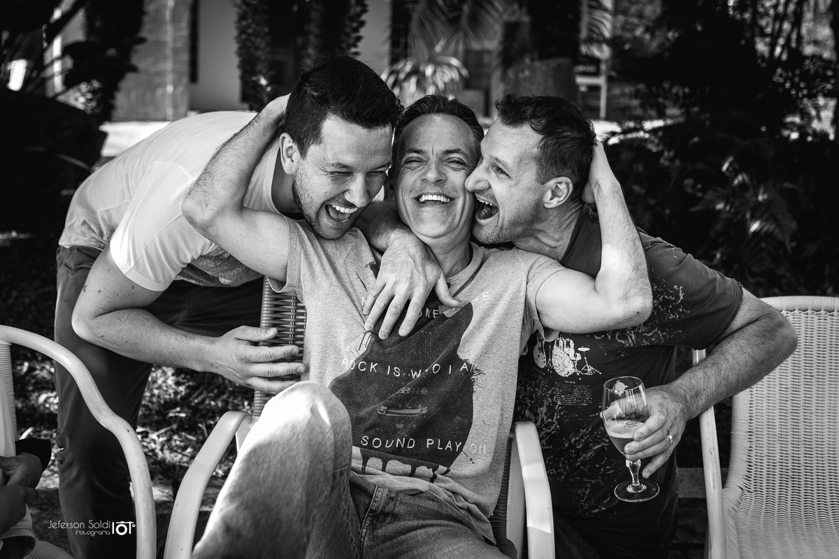 Noivo é abraçado por dois amigos, um de cada lado.