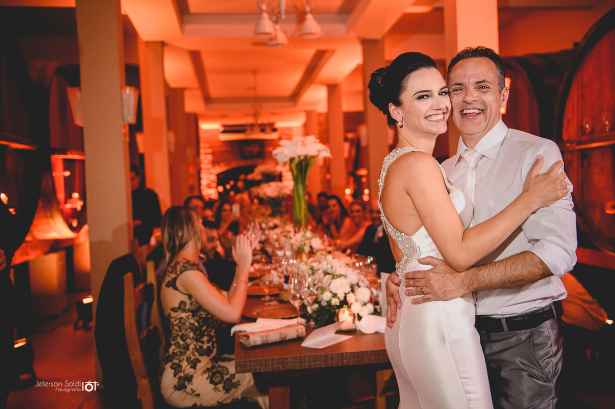 Os noivos abraçados em frente a mesas dos convidados.