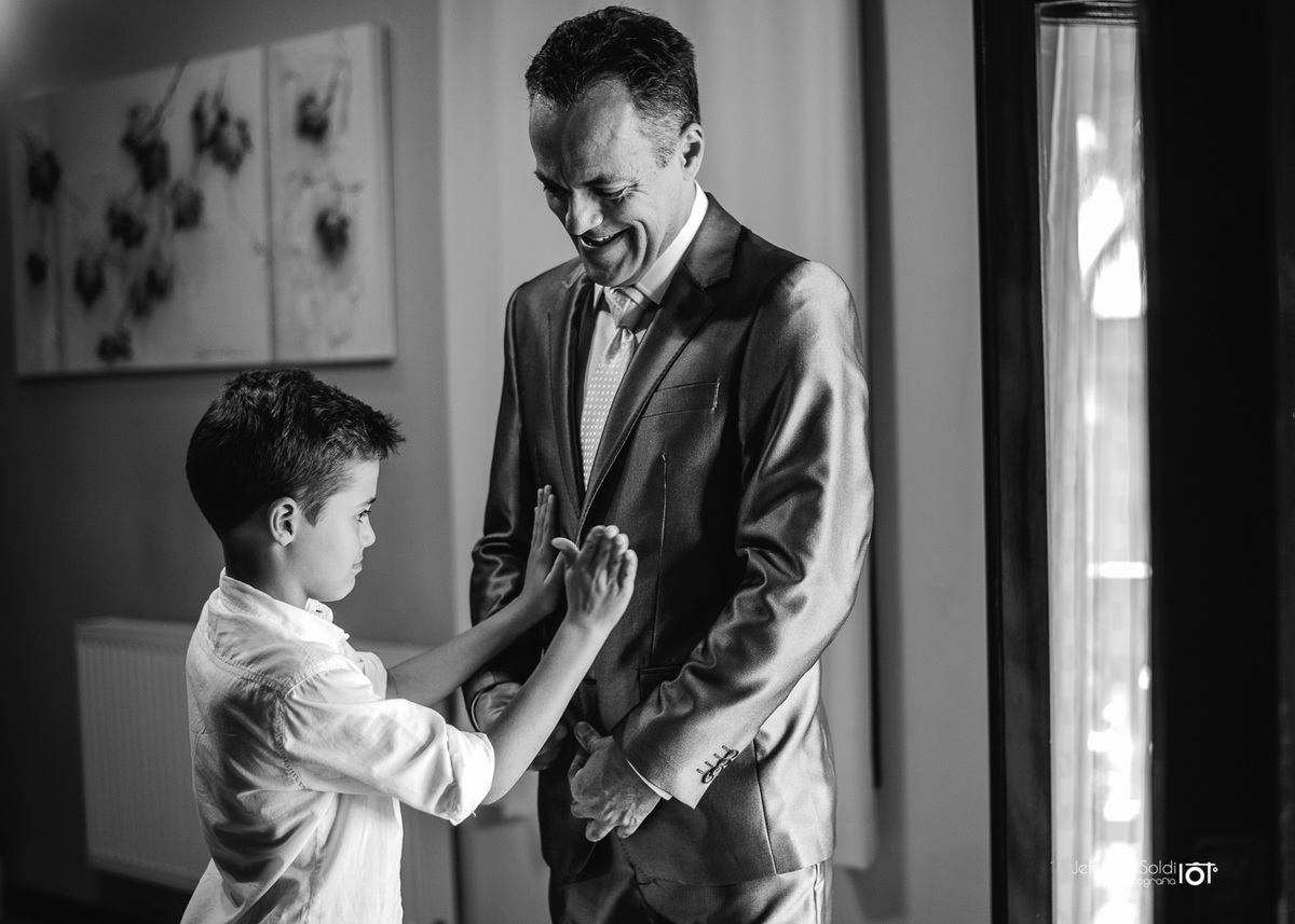 O Filho do casal ajudando o pai a vestir o terno.