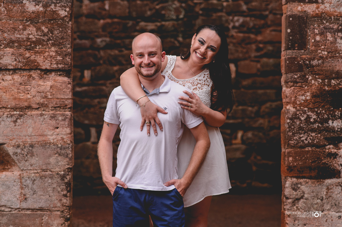 Noiva abraçando o noivo pelas costas no portal das ruínas de São Miguel.