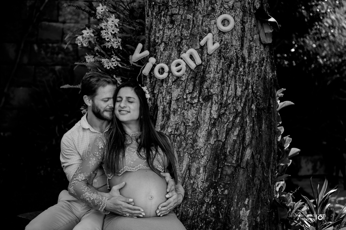 casal abraçados sentados ao pé da árvore com o nome do filho Vicenzo pendurado