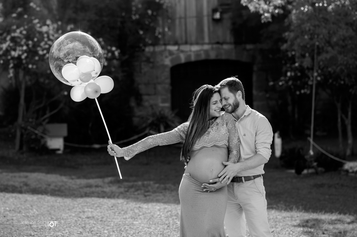 casal gestante abraçadinhos segurando um balão em uma foto preto e branco
