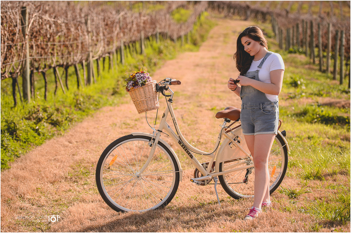 Julia mexendo nos cabelos ao lado de sua bicicleta em meio aos parreirais secos no valo dos vinhedos