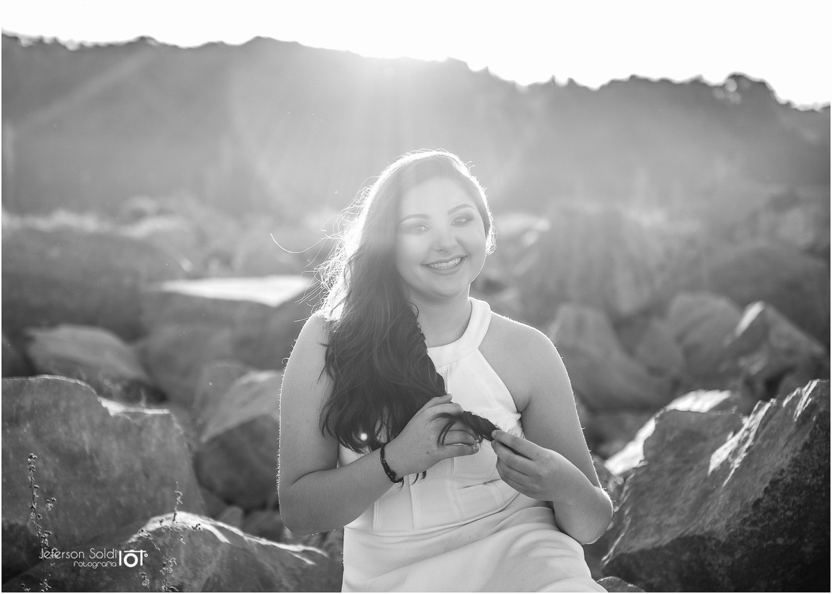Julia mexendo nos cabelos sentada numa pedra sob raios de sol