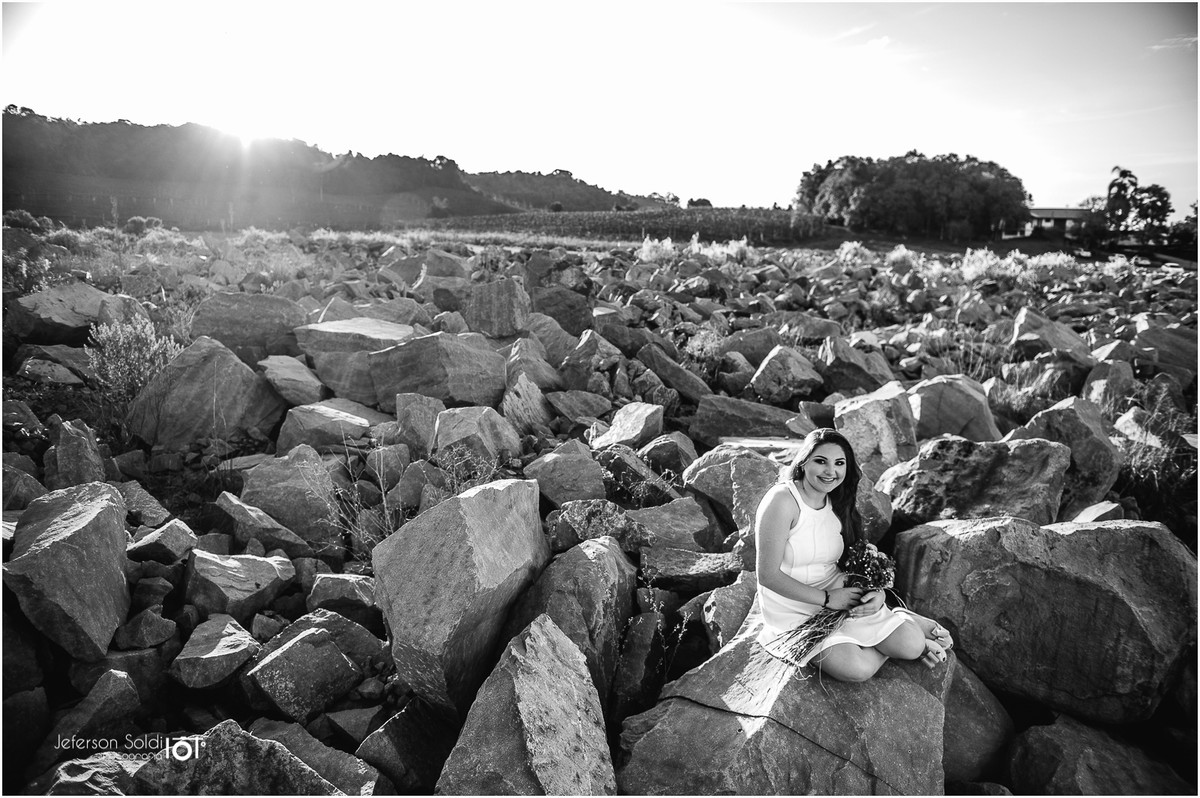 Julia sentada em meio a varias  pedras em preto e branco