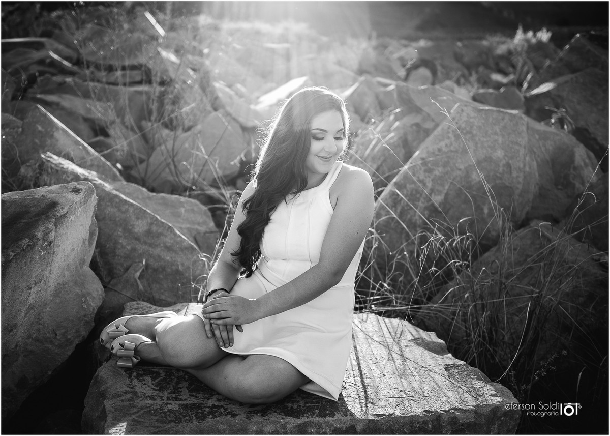 Julia sob reflexo do sol sentada nas pedras