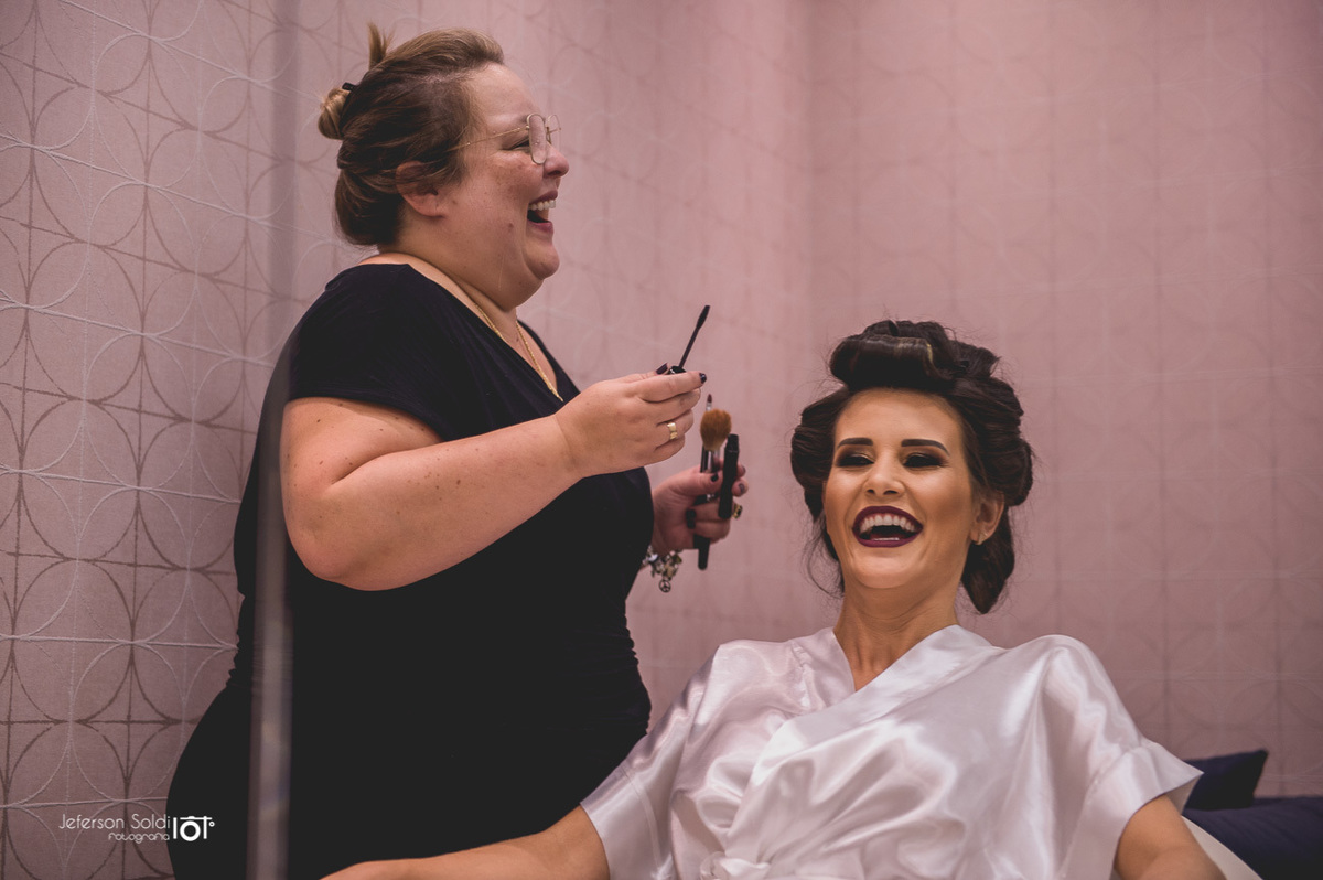 Noiva em um super sorriso expontâneo com a maquiadora.