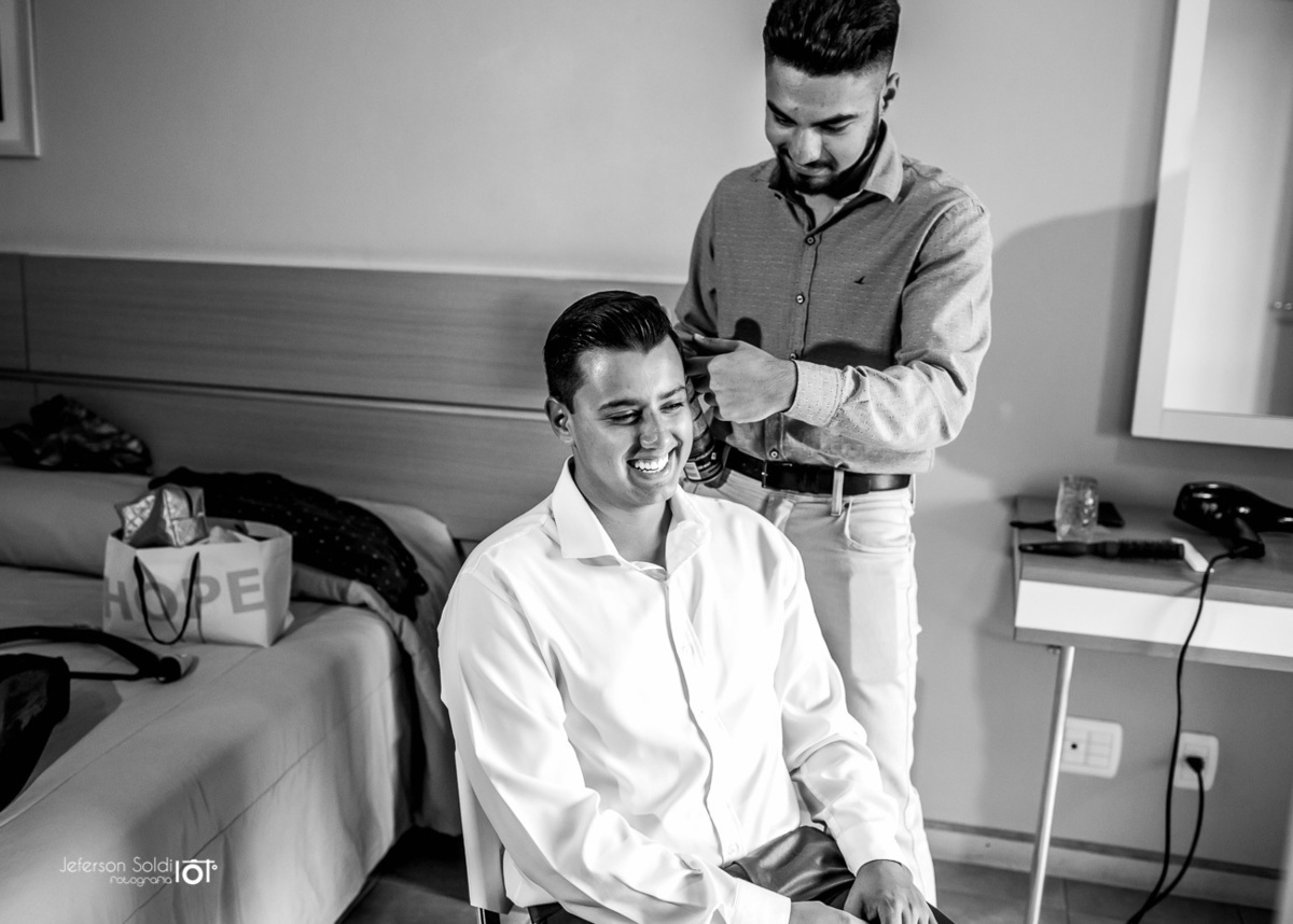 Maquiador ajeitando o cabelo do noivo, foto preto e branco.