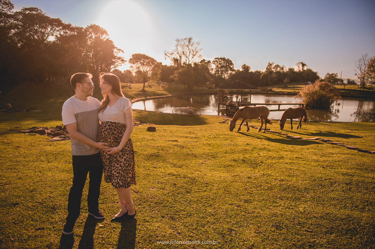 casal de gestantes pousando para foto e no fundo dois lindos cavalos pastando