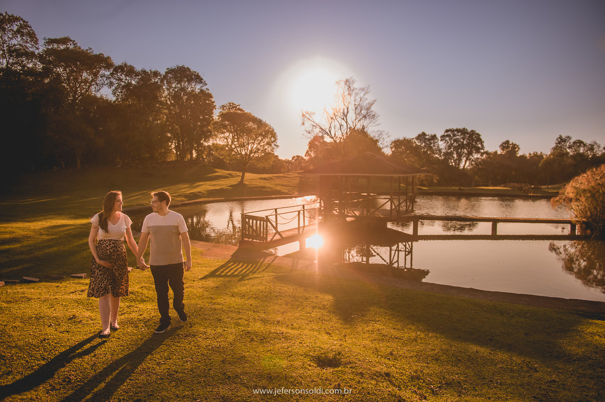 casal de gestante caminhando sorrindo um cenário lindo com lago em um final de tarde magnífico