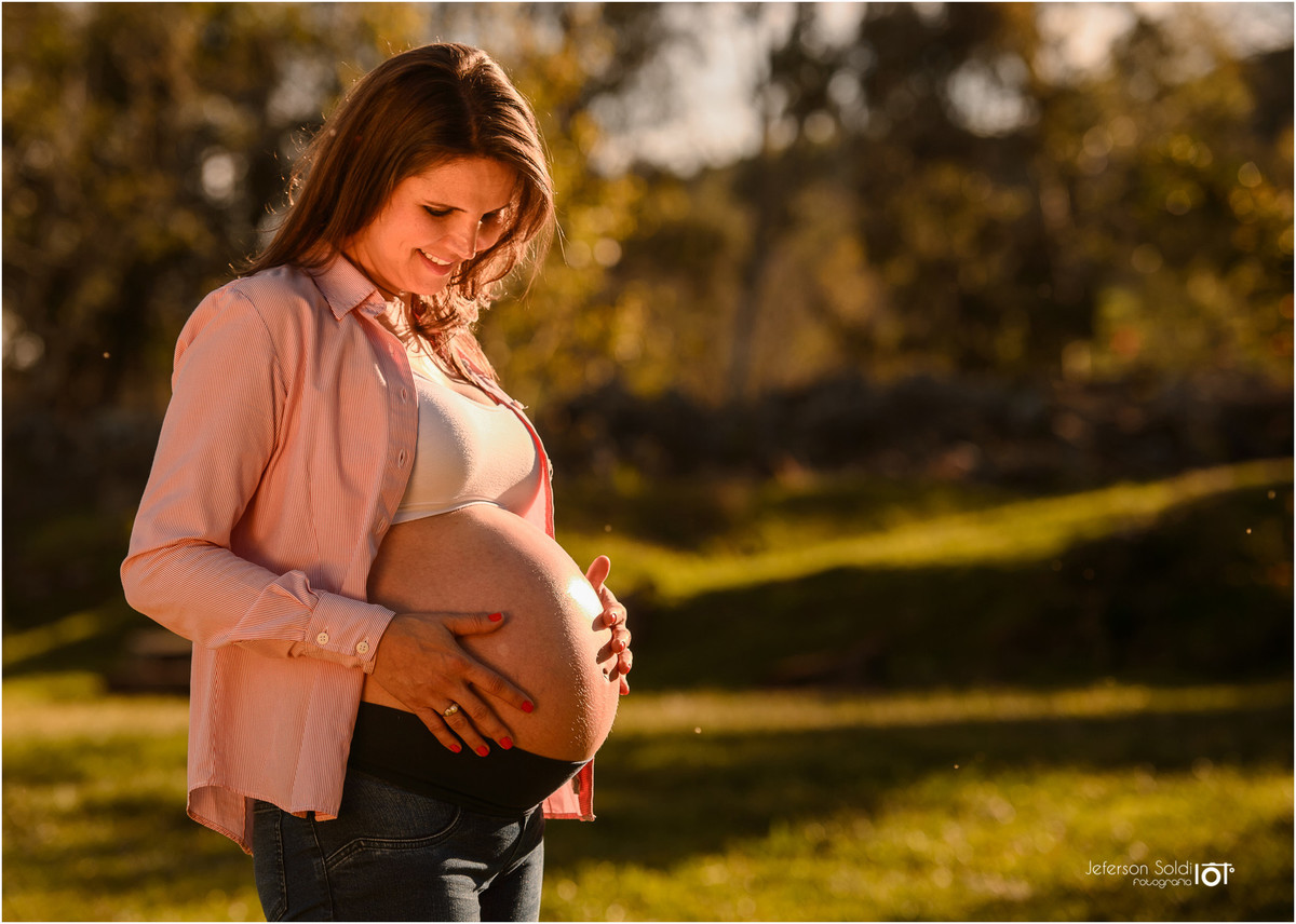 Mãe acariciando a barriga com um cenário lindo ao fundo