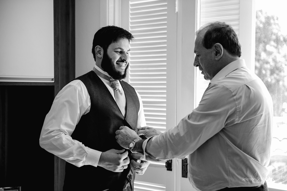 Pai do noivo ajudando a abotoar o colete do noivo