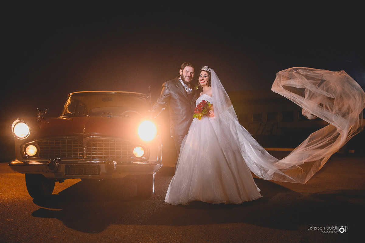 Noivos posando junto ao carro que conduziu a noiva