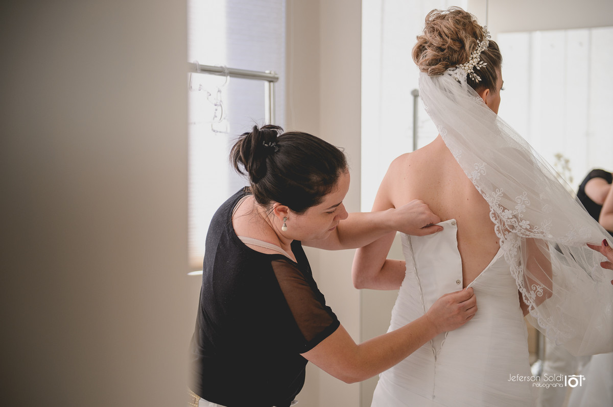 Noiva abotoando o vestido.